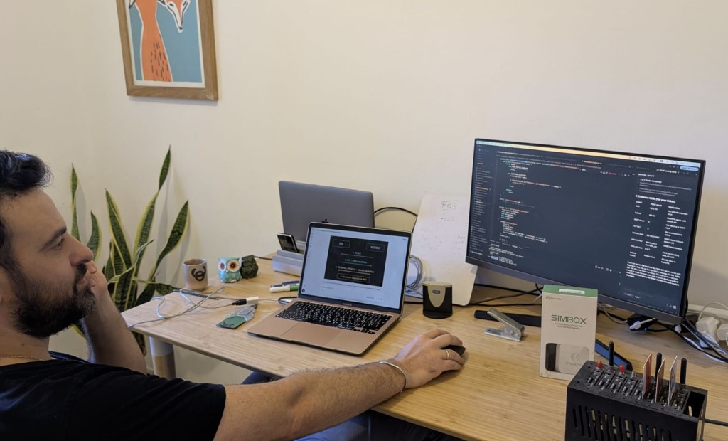 Ariel Hadad at a desk with SIM hardware, a SIM–modem sequence on a laptop, and an evidence table on the monitor